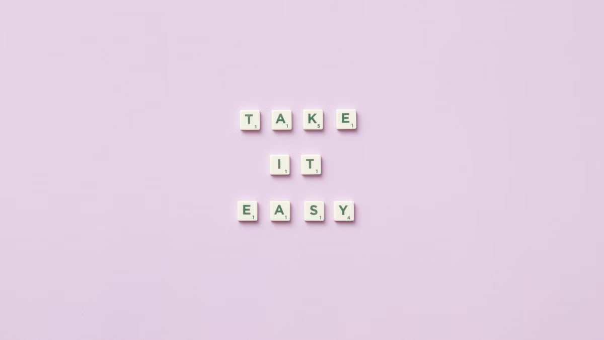Scrabble tiles forming 'Take it easy' against a soft lilac background, evoking relaxation and mindfulness.